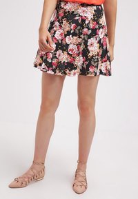 Gonna a pieghe floreale nera con fiori rosa e bianchi. Tessuto leggero, design a pieghe, lunghezza al ginocchio, abbinata a sandali flat con cinturini color nude.