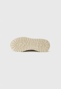 Semelle de chaussure en caoutchouc, avec un motif texturé comportant des rainures profondes et des crampons pour une meilleure adhérence. La couleur est beige clair avec une finition mate.