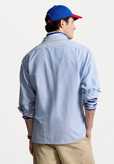 Light blue button-up shirt with long sleeves, rolled cuffs, and a relaxed fit. Worn over a white and blue striped long-sleeve shirt.