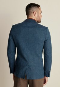 Blazer mit blauem Fischgrätenmuster und taillierter Passform, mit einem Schlitz hinten und schwarzen Knopfakzenten an den Ärmeln.