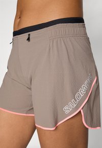 Grå atletiska shorts i en strukturerad tyg, med ett svart elastiskt midjeband och rosa detaljer, samt "SALOMON"-logotypen på sidan.