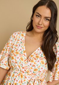 Kukkakuvioinen kietaisumekko V-pääntiellä, jossa on kermanvärinen pohja, oransseja ja keltaisia kukkia sekä lyhyet liehuvat hihat. Sileä kankaan pinta.