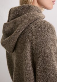 Brązowy sweter z kapturem, fakturowana dzianina, luźny krój, wyrazisty kołnierz, ciepły materiał, miękka faktura, casualowy design, widok z boku.