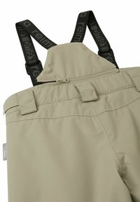 Beżowe wodoodporne ogrodniczki z regulowanymi czarnymi ramiączkami, kieszenią na zamek i wzmocnioną talią dla trwałości. Gładka tkanina o matowym wykończeniu.
