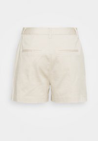 Shorts beige ajustés avec passants de ceinture et deux poches passepoilées au dos, présentés de l'arrière sur un fond uni.