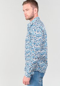 Camicia a bottoni blu e bianca con design fitted, maniche lunghe e colletto a punta, caratterizzata da diverse fantasie floreali in tutto il capo.