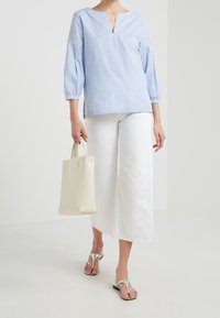 Blouse rayée bleu clair avec un col en V, manches 3/4, associée à un pantalon large blanc et un sac fourre-tout crème, accessoirisée avec des sandales argentées.