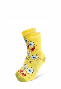 Calzini gialli con stampe ripetute di personaggi dei cartoni animati, che mostrano occhi blu e bocche rosse, con una trama liscia e polsini elastici.