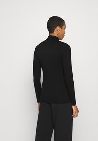 Black turtleneck long-sleeve top made of smooth fabric, featuring a fitted silhouette and a high neckline, paired with loose black pants.
