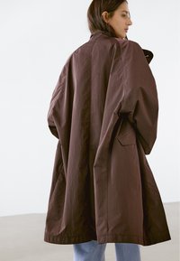 Brun oversized jacka i lättviktigt tyg, med hög krage och lös passform, samt subtil textur och sidofickor.