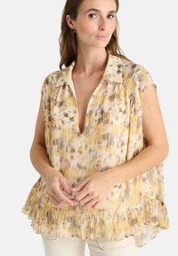 Blusa de estampado floral con escote en V profundo, mangas cortas tipo capa y dobladillo con volantes. Hecha de una tela ligera en tonos de amarillo y verde.