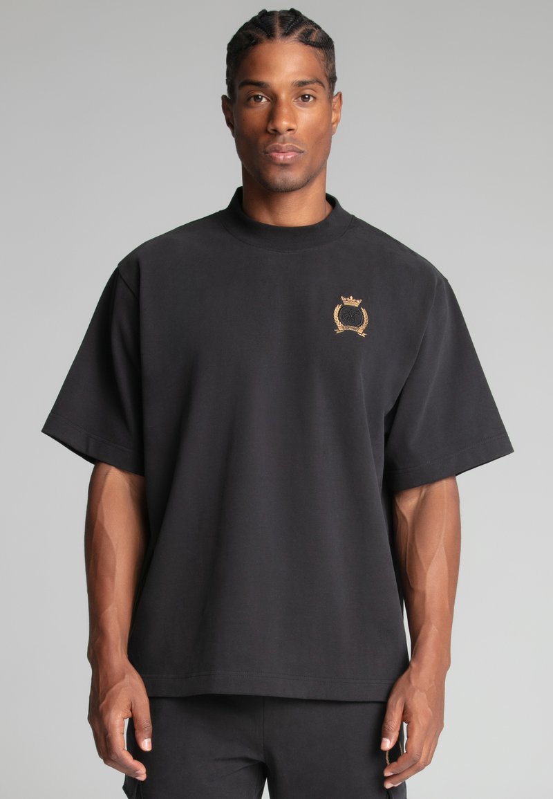 Sort oversized t-shirt lavet af bomuld, med korte ærmer, høj hals og et guld broderet logo på venstre bryst.