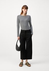 Langermet svart og hvitstripet topp paret med høyt liv, bred ben bukser i svart. Tilbehør inkludert en svart håndveske og grønne sandaler.