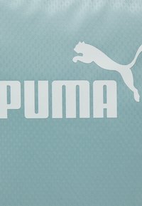 Vaaleansininen teksturoitu tausta, jossa on valkoinen "PUMA"-teksti ja loikkaavan pumana kuusi. Suunnittelussa korostuu geometrinen kuvio.