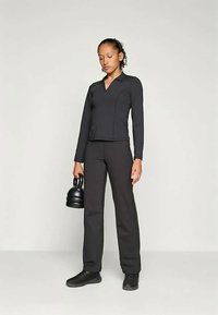 Μαύρη αθλητική ενδυμασία που περιλαμβάνει μια εφαρμοστή μπλούζα με μακριά μανίκια και V-λαιμόκοψη, καθώς και παντελόνι. Το μοντέλο κρατάει μια μαύρη kettlebell.