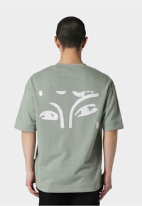 Kortærmet mintgrøn t-shirt i bomuld med et stort hvidt abstrakt design på ryggen. Afslappet pasform med blød tekstur og sænkede skuldre.