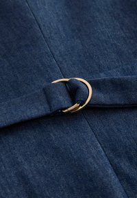 Tamnoplavi trapera tkanina sa zlatnom metalnom D-prstenom koji pričvršćuje odgovarajući trakasti remen od trapera.