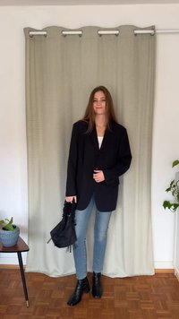 Blazer negro extragrande con un solo botón, combinado con jeans pitillo azul claro y botines negros. Sosteniendo un bolso pequeño negro.
