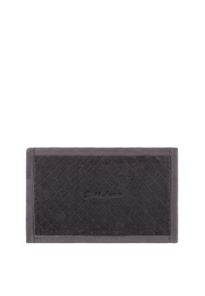 Tapis de bain rectangulaire gris foncé avec un motif matelassé en losange et un logo brodé discret au centre, posé sur un fond blanc.