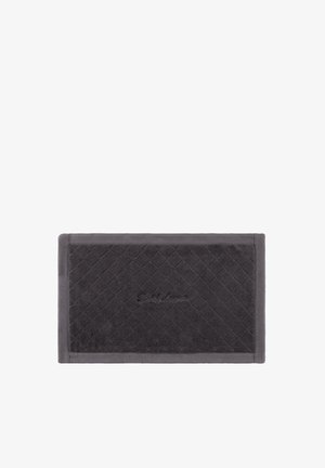 Tapis de bain rectangulaire gris foncé avec un motif matelassé en losange et un logo brodé discret au centre, posé sur un fond blanc.
