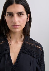 Blouse noire avec des détails en dentelle intricats sur les épaules, un décolleté en V et un tissu doux et texturé.