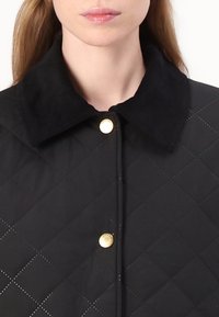 Black quilted jacket featuring a soft, textured collar and gold hardware accents. The fabric has a diamond pattern and is lightweight.