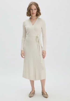 Wickelkleid aus cremefarbenem, geripptem Stoff, mit langen Ärmeln, V-Ausschnitt, einem Bindegürtel in der Taille und einem knielangen Rock. Weicher Stoff, minimalistisches Design.