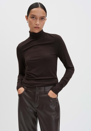 Haut à col roulé long brun en tissu doux et extensible. Le mannequin le porte avec un pantalon en cuir brun foncé taille haute.