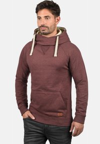 Maroon hoodie with a large cowl neck, cream drawstrings, kangaroo pocket, and a textured finish. Features a small leather logo on the hem.