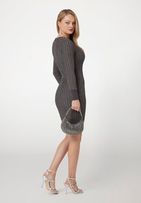 Grijze ribbeljurk met lange mouwen, slim fit. Gepaard met zilveren bandjeshakken en een kleine, versierde handtas. Glad textuur.