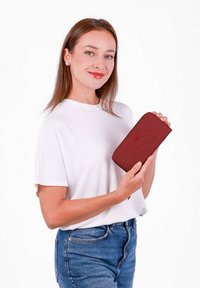 Red zippered wallet with a textured fabric surface, held in hand. The wallet features a simple design with subtle branding in the center.