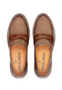 Mocasines de cuero marrón con una textura suave, que presentan acentos en marrón oscuro contrastantes y costuras decorativas. Logo de Pikolinos en la plantilla.