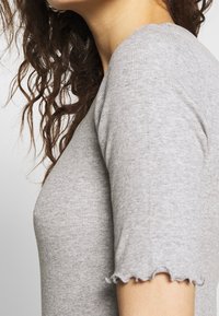 Camiseta gris de canalé con mangas cortas y dobladillo ondulado. La vista en primer plano enfatiza la suavidad de la textura y la forma ajustada.