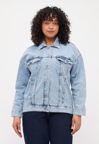 Chaqueta de mezclilla azul claro con dos bolsillos en el pecho, botones a presión plateados y un corte relajado. Presenta un cuello clásico y una textura ligeramente descolorida.