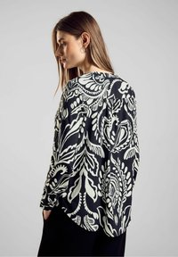 Blusa a maniche lunghe a righe bianche e nere, con vestibilità ampia e disegni floreali, texture morbida e orlo curvo.