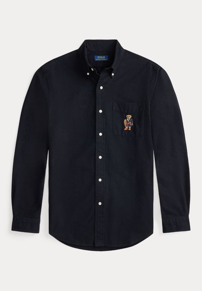 Ναυτικό μπλε βαμβακερό πουκάμισο με κουμπιά και μία τσέπη στο στήθος, που διαθέτει κεντημένο σχέδιο αρκούδας με καρό ντύσιμο.