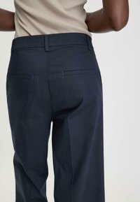 Meripura teka navy dengan tekstur halus, dilengkapi dengan dua saku belakang dan desain kaki lurus. Detail jahitan yang halus di sepanjang pinggang.