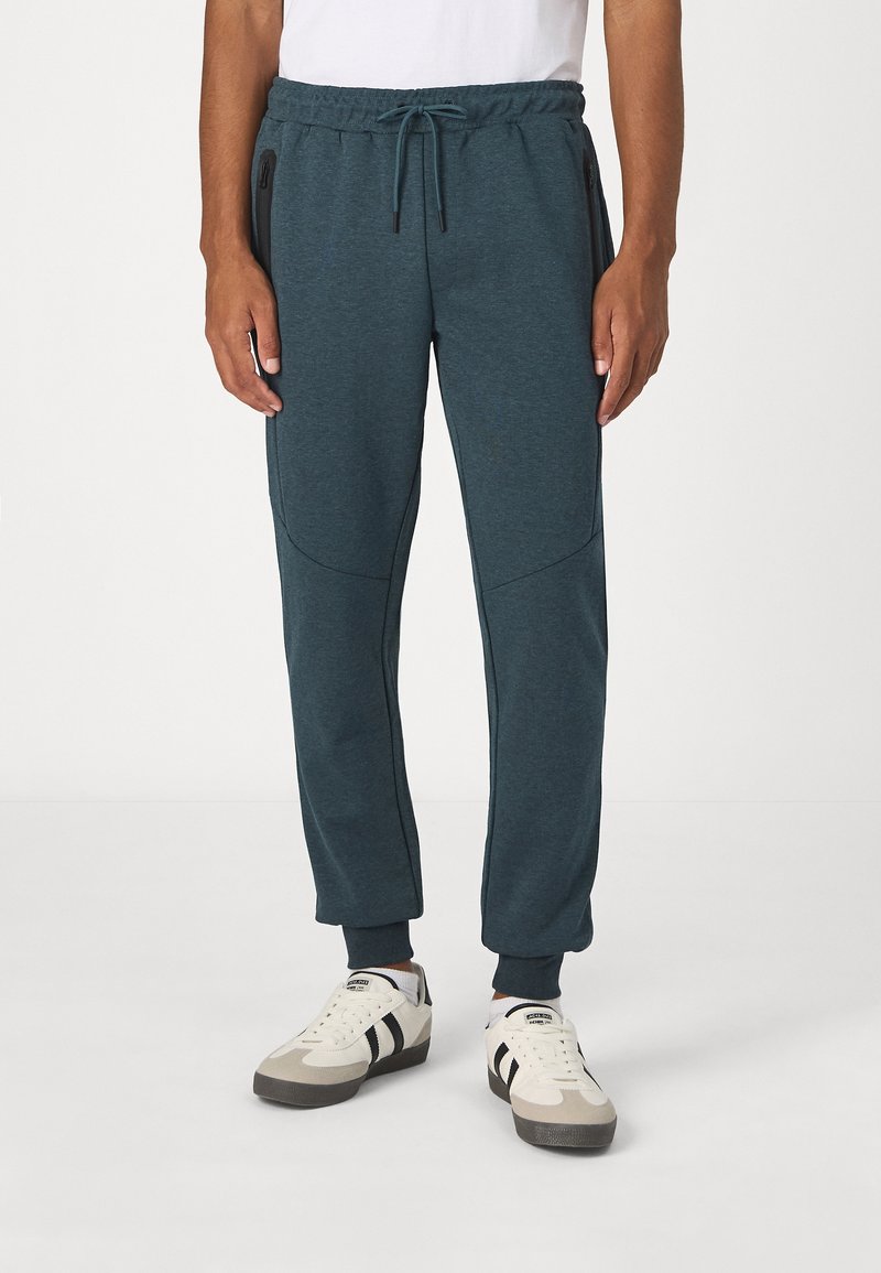 Donkerblauwe joggers met een elastische tailleband, een trekkoord, zijzakken met rits en taps toelopende boorden. Gemaakt van een zachte, textuurstof.