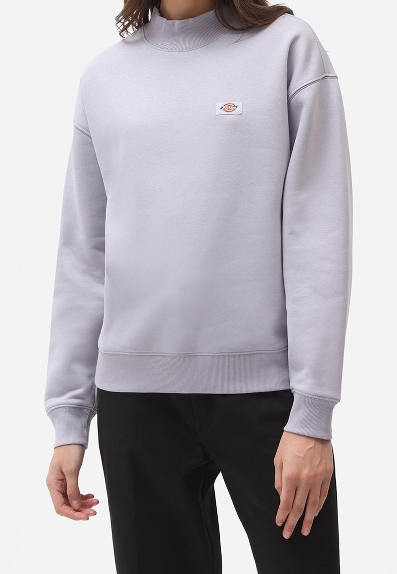 Ljusgrå sweatshirt med hög krage, ribbade ärmslut och nederkant. Har en liten logotypapplikation på bröstet. Tillverkad av ett texturerat tyg.