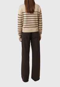 Beżowo-brązowy sweter w paski z długimi rękawami, z prążkowanym dołem, zestawiony z luźnymi, ciemnobrązowymi spodniami.