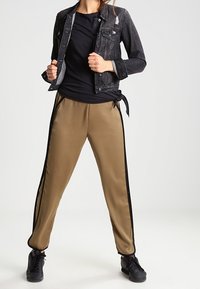 Giacca di jeans nera con strappi, t-shirt nera e joggers in satin beige con strisce nere laterali, abbinati a sneakers nere.