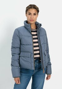 Pufferjack in lichtblauw met een hoge kraag, frontzipper en zijzakken. Kenmerkt zich door horizontale quilted-stiksels en contrasterende tan accenten.