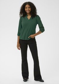 Top verde cu nervuri, cu decolteu în V și mâneci trei sferturi, asortat cu pantaloni negri evazați și balerini negri. Textură netedă.