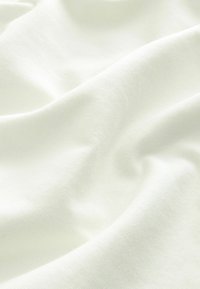 Puha krémszínű textil, sima, enyhén struktúrált felülettel, lágy redőkkel és leomló formákkal.