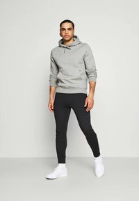 Grauer Hoodie mit Kordelzügen, getragen mit schwarzen, eng anliegenden Leggings. Das Modell trägt weiße Sneakers, insgesamt mit einer glatten Textur.