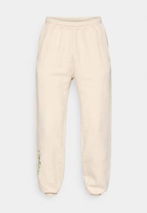 Pantalon de survêtement de couleur crème en tissu doux, doté d'une ceinture élastique, de poches latérales et d'une broderie florale sur la jambe gauche.
