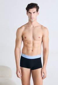 Zwarte boxershorts met een lichtblauwe tailleband met het logo "Calvin Klein". De stof lijkt soepel en aansluitend, waardoor de lichaamsvorm van het model goed zichtbaar is.
