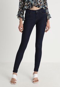 Jeans skinny azul oscurecidos en denim elástico con una textura suave, cintura alta, diseño de cinco bolsillos y sutiles detalles de costura.