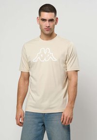 Béžové tričko s krátkym rukávom z mäkkej bavlny, na hrudi s bielym grafickým logom. Voľný strih s okrúhlym výstrihom.