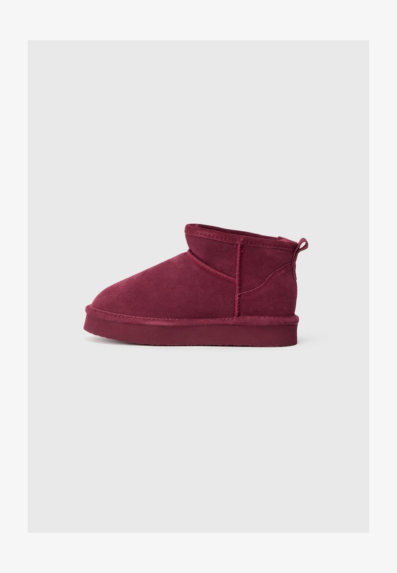 Botas de tornozelo em camurça bordeaux com biqueira arredondada, golinha curta e alça na parte de trás, apresentando detalhes em costura e sola plana.